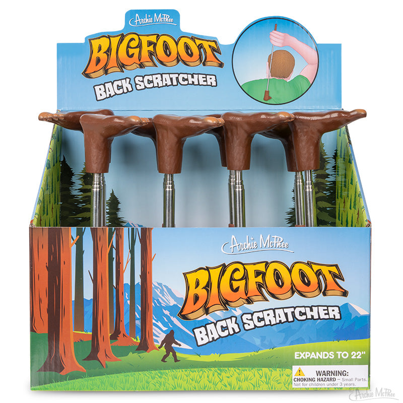 Box display of Bigfoot Back Scratcher novelty items featuring brown feet handles and forest-themed packaging.