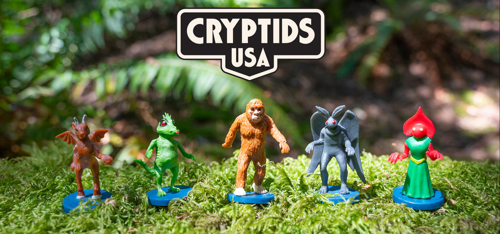 Five cryptid figurines stand on moss under a Cryptids USA sign.